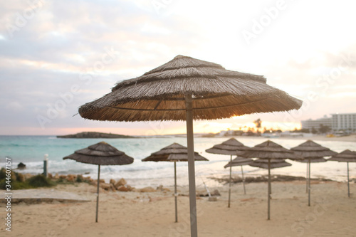 beautiful straw umbrellas on the beach on the empty beach, bright blue water and sky, paradise tropical beach,relaxing time,,amazing view,no people, sunset background. selective focus © Andriy Medvediuk