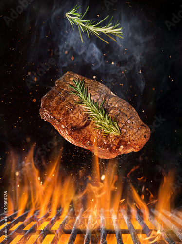 Tasty beef steak flying above cast iron grate with fire flames. Freeze motion barbecue concept.