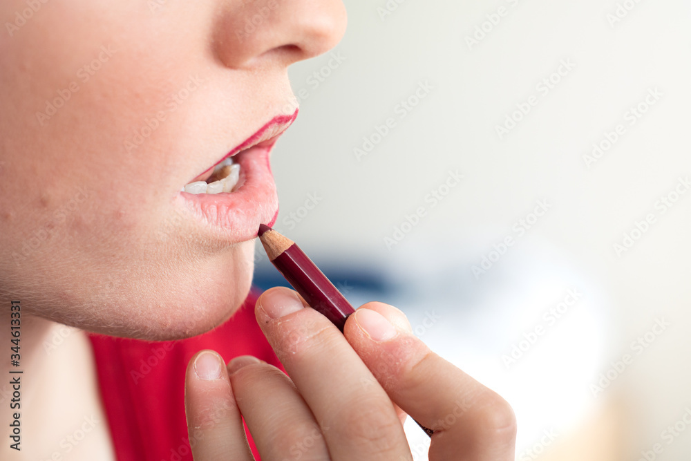 Caucasian while young female applying red crayon make up on her lips close up shot unrecognizable
