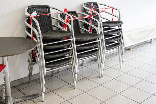 Fototapeta Naklejka Na Ścianę i Meble -  Stacks of chairs locked with red and white barricade tape in an empty ice cream parlor, during the coronavirus pandemic, due to the danger of infection the gastronomy is closed, copy space