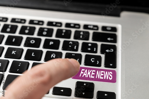 Fake News words on keyboard button. A finger pressing a colored button on notebook