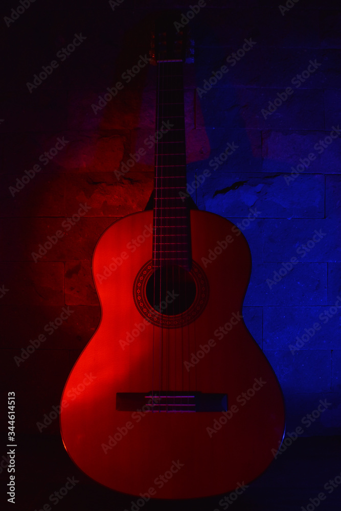 Acoustic guitar leaning against a wall with colored lights. Guitar on stage lighting. Music