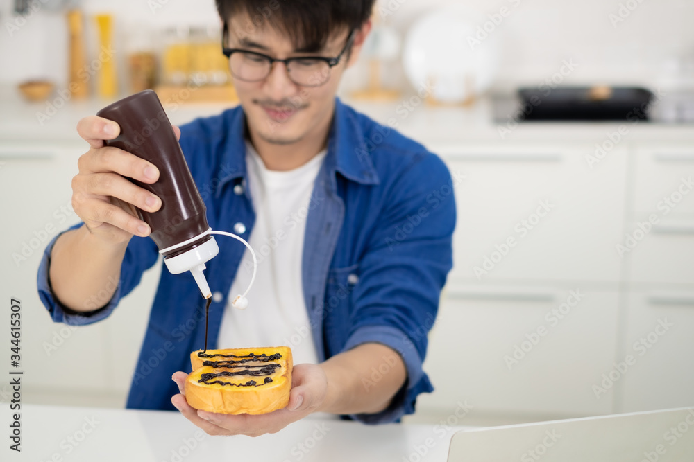 Asian freelance young man pour chocolate on bread for breakfast in white kitchen Asian freelance young man pour chocolate on bread for breakfast in white kitchen