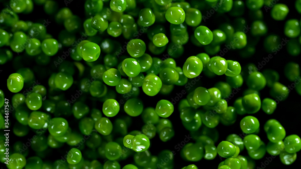Fresh green peas exploding on black background, freeze motion.