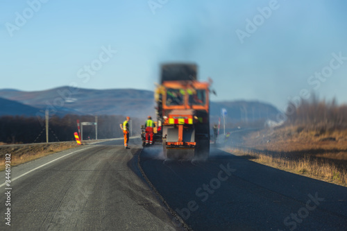 Asphalt paver machine and steam road roller during road construction and repairing works, process of asphalting and paving, workers working on the new road construction site, placing a layer