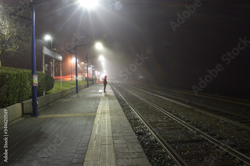 Night view of outdoor train station. Foggy and misty. One man standing on platform, red jacket.
