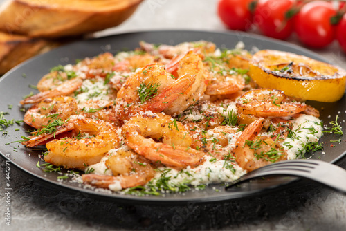 selective focus of fried shrimps in sauce with dill and lemon in black plate on grey concrete background