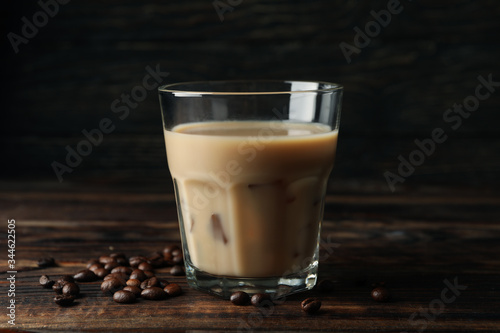 Glass of ice coffee on wooden background. Coffee seeds