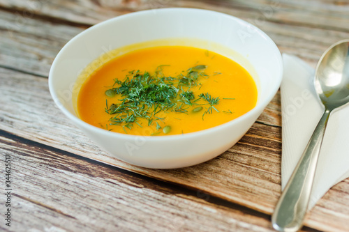 Traditional pumpkin soup with seeds, dill on a wooden table close up.
