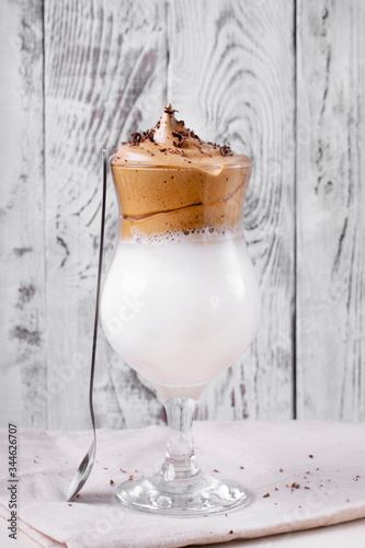 Whipped dalgona coffee in a tall glass against the white wooden background