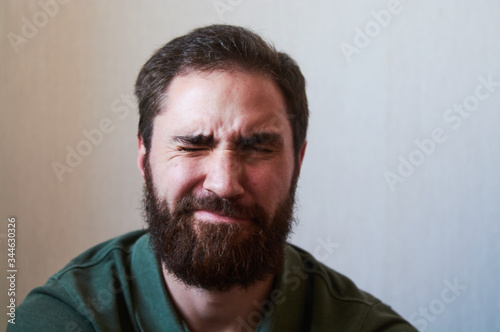 Portrait of young guy with dark beard with various emotions on his face in green shirt. © Vlada
