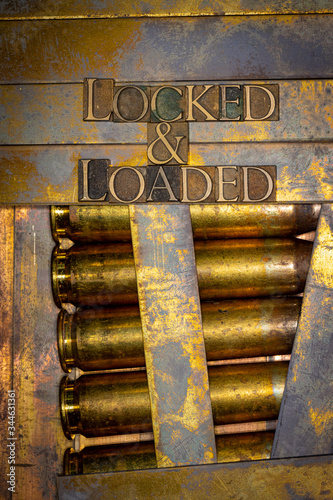 Photo of real authentic typeset letters forming Locked and Loaded text on vintage textured grunge copper and gold background with 50 cal bullet casings