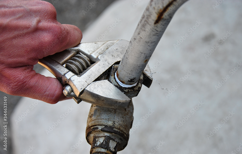 
plumbing wrench in hand and old water tap