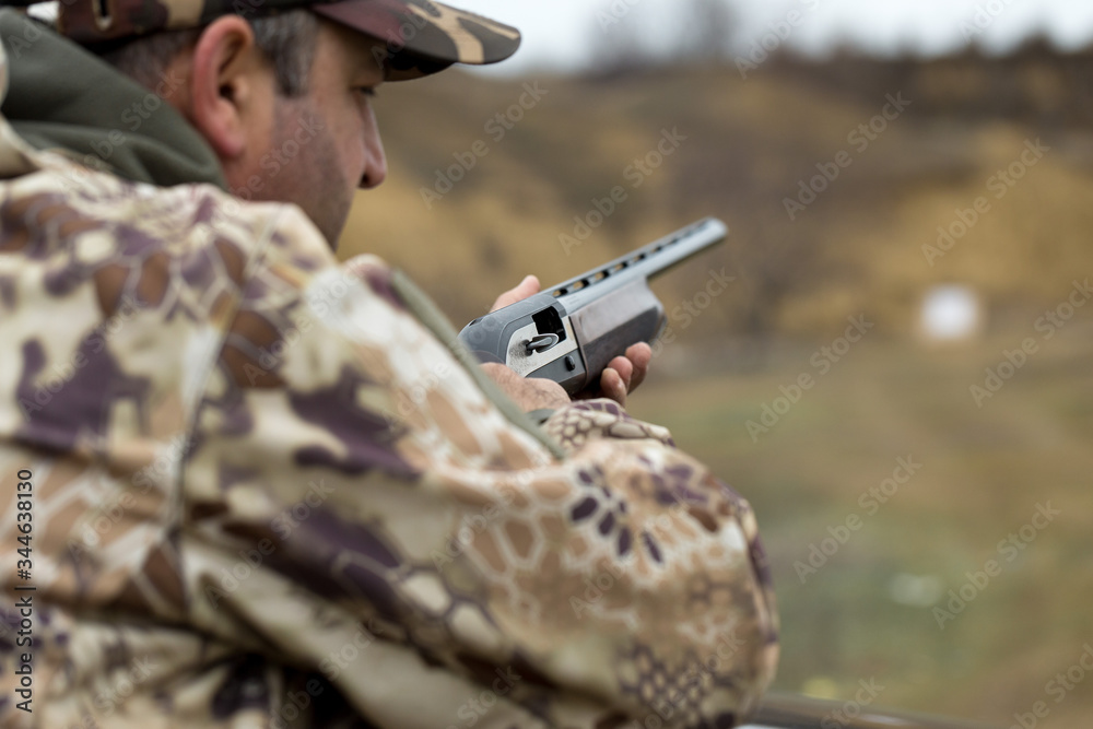 Fototapeta premium A hunter in camouflage at the shooting range calibrates the weapon. A man shoots at targets.