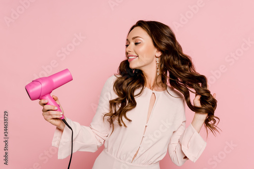 Photography cheerful young woman using hair dryer isolated on pink
