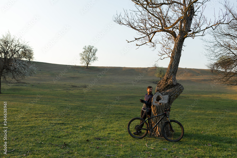 Naklejka premium Cyclist in shorts and jersey on a modern carbon hardtail bike with an air suspension fork standing on a cliff against the background of fresh green spring forest