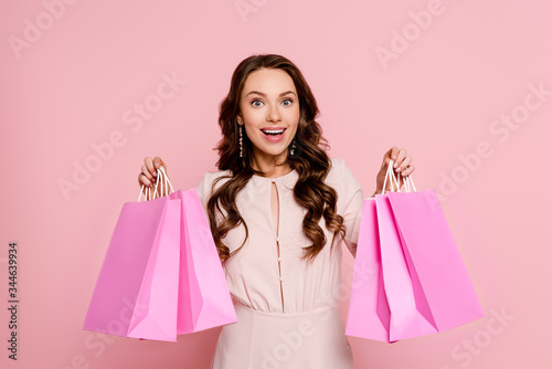 excited young woman holding shopping bags isolated on pink