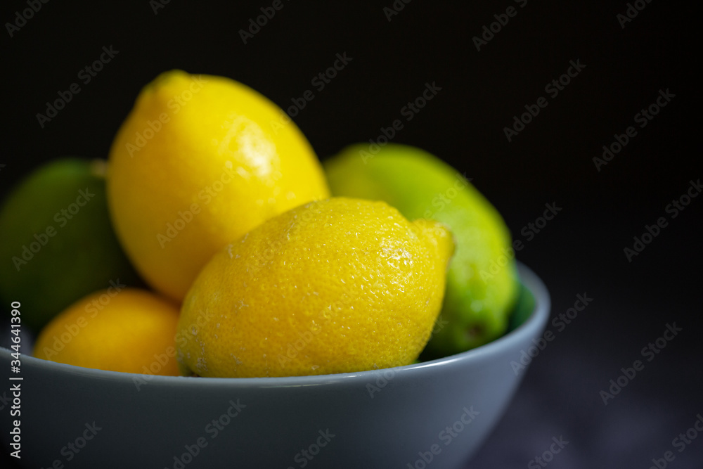 A lot of citrus fruits in a blue bowl on the dark background. Fresh lemons in a bowl. Close up of the lemons on the dark background. Lemons and limes A lot of citrus fruits in a blue bowl on the dark background. Fresh lemons in a bowl. Close up of the lemons on the dark background. Lemons and limes