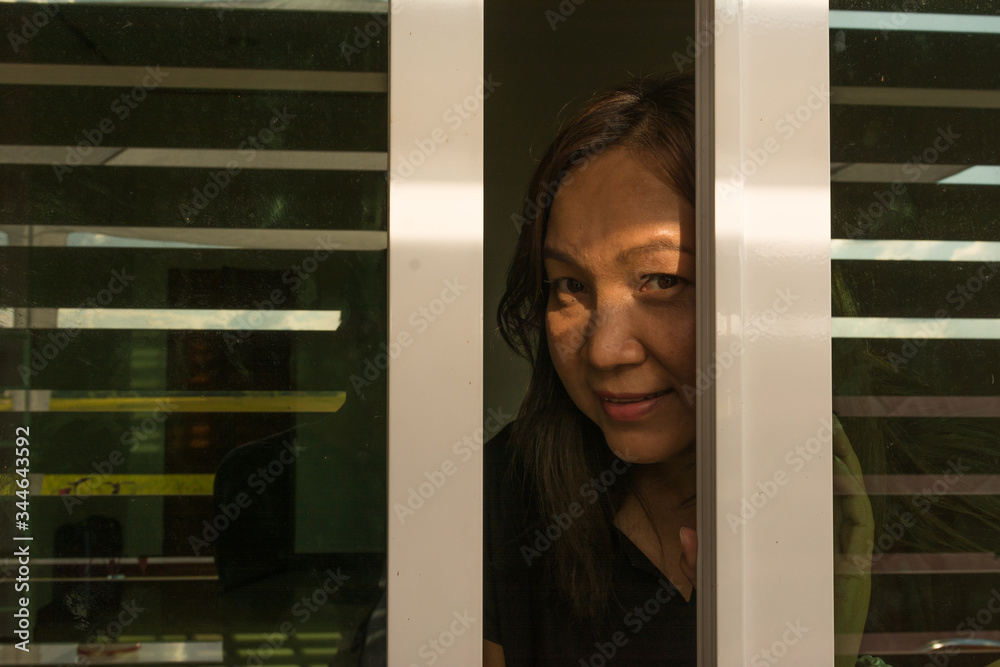 Young Asian woman looking out the stip window behind the dark room. Young Asian woman looking out the stip window behind the dark room.