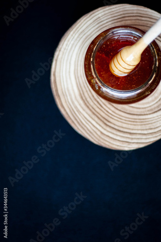 Wooden spoon drowning in to the glass jar with honey.