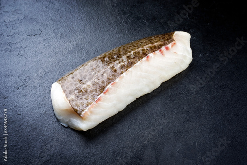 Fototapete Raw Norwegian skrei cod fish filet with skin as closeup on black board with copy