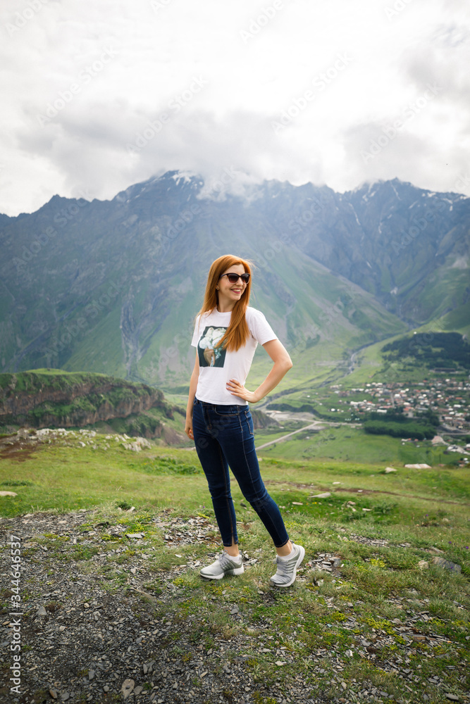 young beautiful girl with a blonde in a white t-shirt stands on a background of mountains in Georgia
