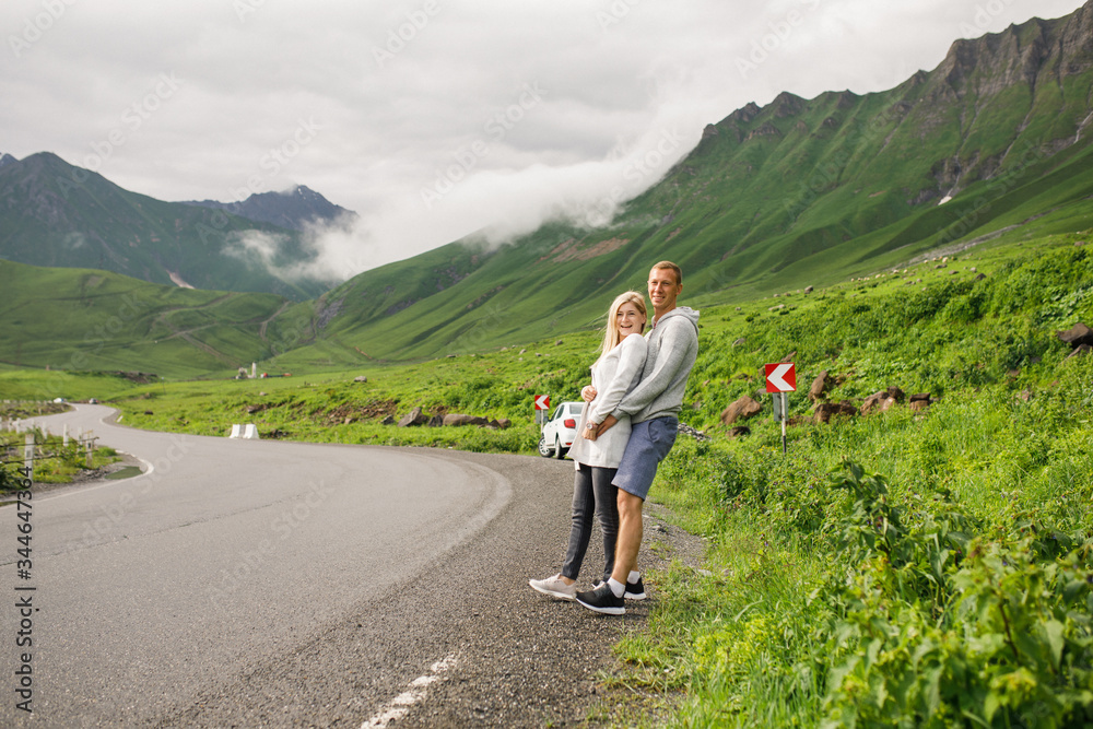 young beautiful couple travelers stand on the road against the backdrop of the mountains
