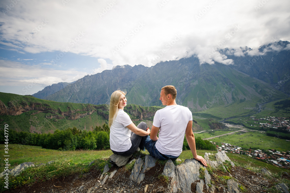 Naklejka premium young beautiful couple travelers girl blonde in a white t-shirt, a man in a white t-shirt stand on a background of mountains in Georgia