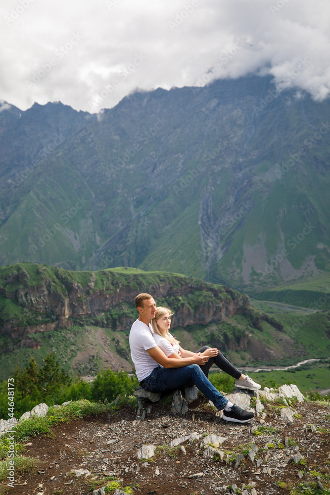 young beautiful couple travelers girl blonde in a white t-shirt, a man in a white t-shirt stand on a background of mountains in Georgia
