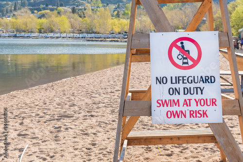 No lifeguard warning sign on sandy beach with view of water photo