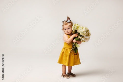 Stylish little girl in yellow dress holding bouquet of wild flowers isolated at the white background. Child fashion. Copy space