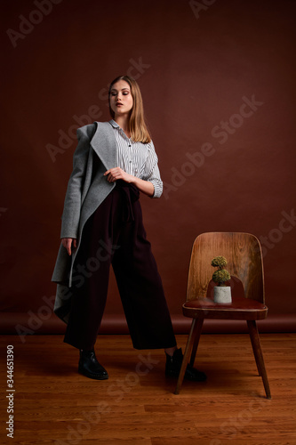 Gorgeous young female in classic suit, black shoes and grey coat. Vintage chair. Woman's clothes.