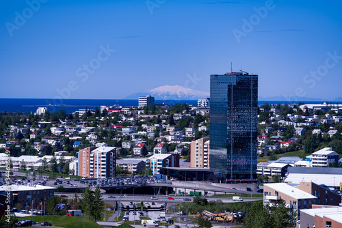 The view of Kópavogur, Iceland in the outskirts of Reykjavik.  The magnificent glacier Snæfellsjökull is seen in the distance across the water. A glass skyscraper in the foreground. © KatalysatorAV