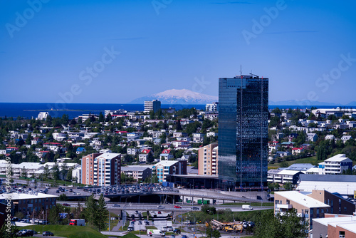 The view of Kópavogur, Iceland in the outskirts of Reykjavik.  The magnificent glacier Snæfellsjökull is seen in the distance across the water. A glass skyscraper in the foreground. photo