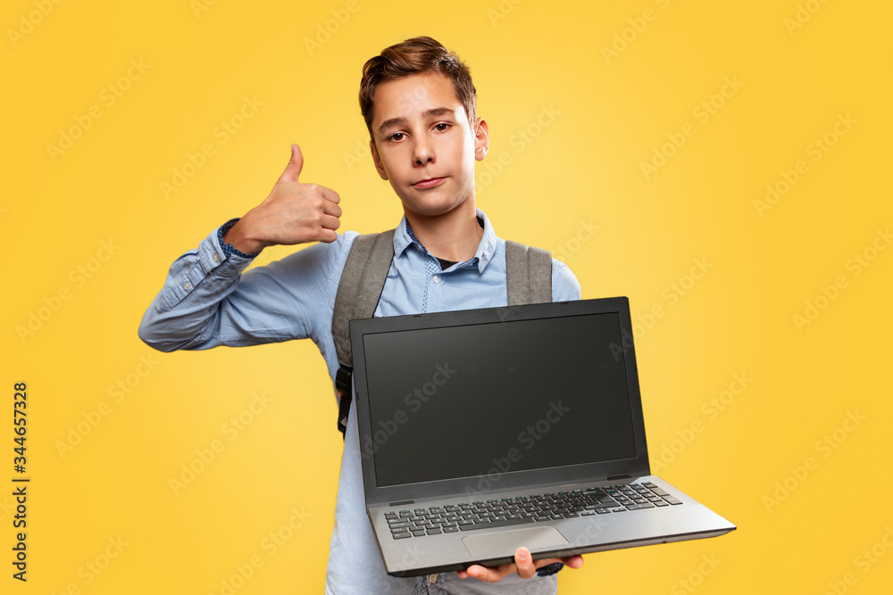 Concept of modern technologies and education. Caucasian teen boy holding open laptop and showing thumbs up. Yellow background. Copy space Concept of modern technologies and education. Caucasian teen boy holding open laptop and showing thumbs up. Yellow background. Copy space