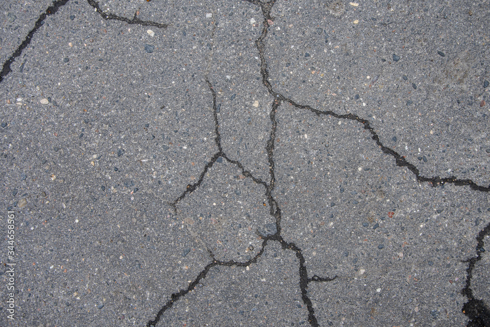 Fototapeta premium Cracked asphalt in the city, cracks and potholes on the road, textured road surface, selective focus.