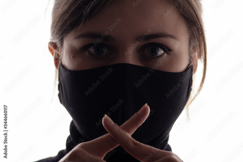 young woman face in a black protective mask showing a gesture of silence with two crossed fingers on her mouth, concept of silence of the truth, secret information young woman face in a black protective mask showing a gesture of silence with two crossed fingers on her mouth, concept of silence of the truth, secret information