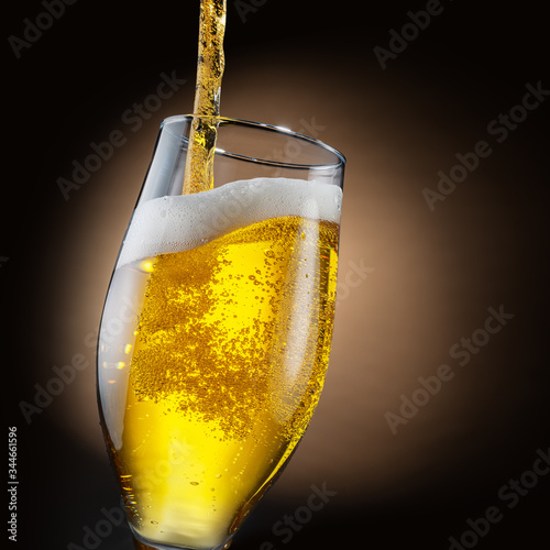 Jet of beer is poured into a beer glass, causing a lot of bubbles and foam.