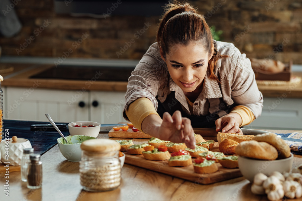 Smiling woman making bruschetta with healthy ingredients in the kitchen.