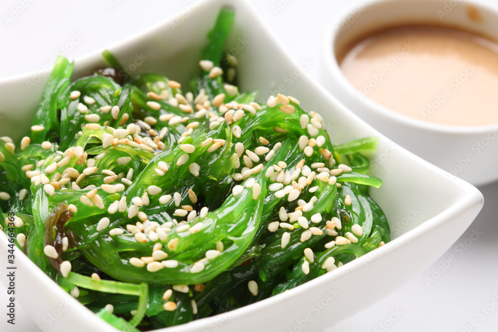 Japanese hiyashi wakame chuka salad with white sesame seeds and peanut sauce in a bowl on a white background.