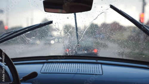 POV from the front seat to windshield of old retro car during bad weather. Wipers removing raindrops from the window of vintage automobile during ride on the highway. Close up Slow motion