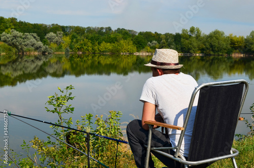  a fisherman sits on a chair and a fisherman in front of a pond fishing, Fishing on a pond on a warm day, fishing rods and feeders are thrown into the water Fishing adventures,fisherman,