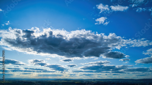 Blue sky and multiple clouds background showing a horizon and a hidden sun © Greg Kelton
