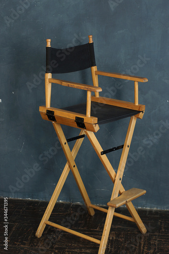 A filmmakers chair with wooden legs and a black seat stands against a gray-blue wall