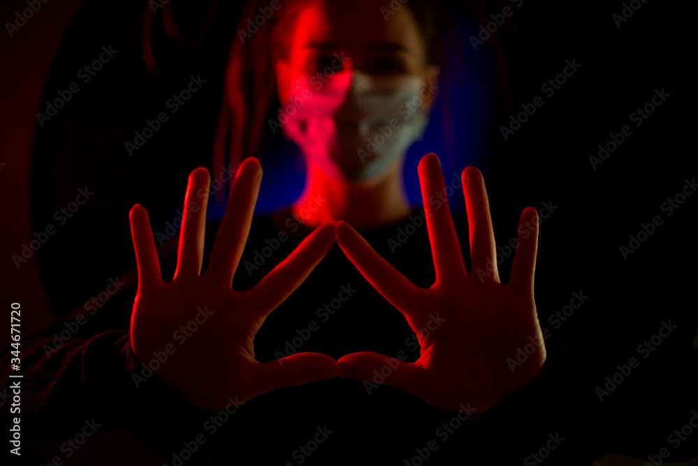 Medical worker in a medical mask in defocused. medic girl in a dark room with a red and blue light. during the coronavrus pandemic. Health with Hands.