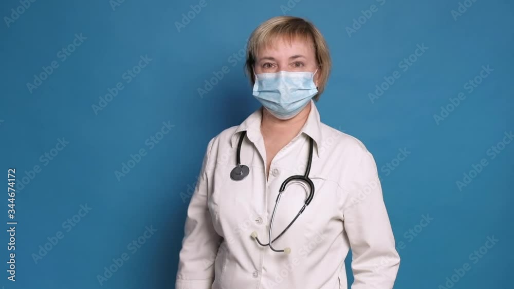 Eldery caucasian doctor lady in white coat on blue background. She wear stethoscope and points her finger Eldery caucasian doctor lady in white coat on blue background. She wear stethoscope and points her finger