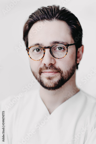 Fototapeta Naklejka Na Ścianę i Meble -  Portrait of handsome doctor brunet man in white coat in medical office with glasses. brutal and handsome man.