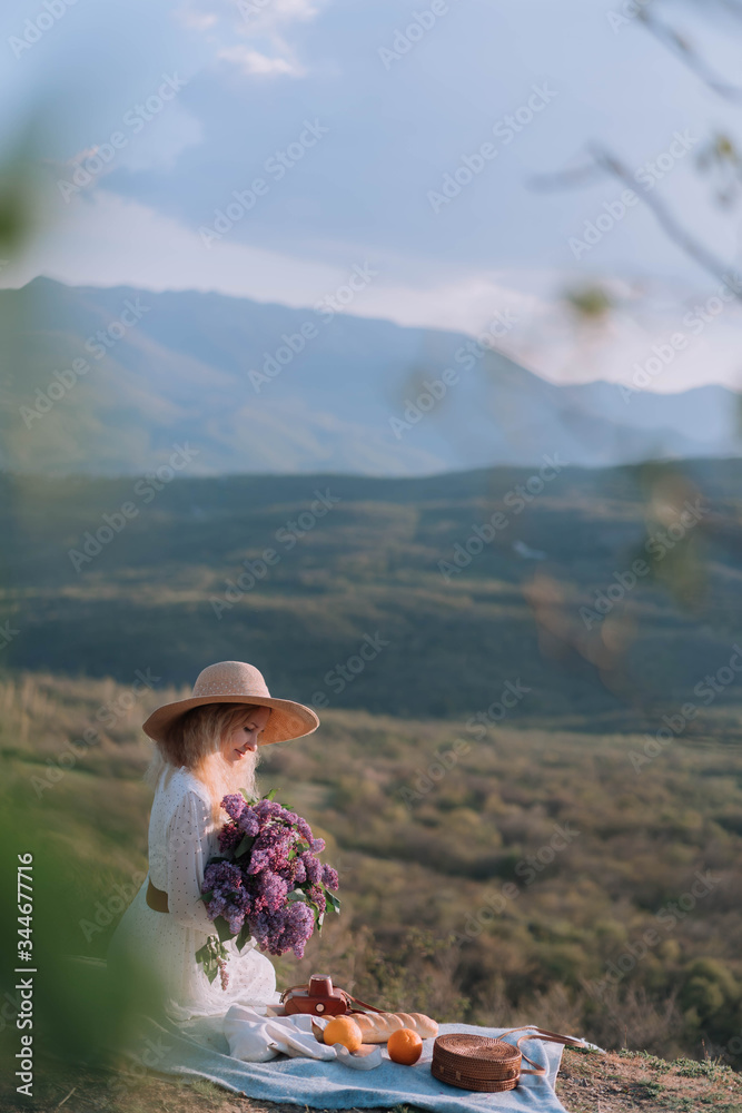Stylish woman in a straw hat posing on lilac flowers on a background of mountains.