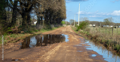 A rural country road full of chuckholes, potholes, and disrepair holds water after an overnight rain. It could use some repair work and loads of gravel. photo