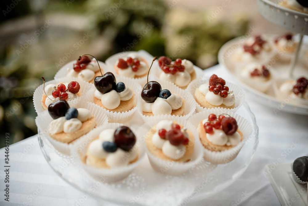 Many cupcakes decorated with cream and berries on a plate